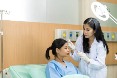 Asyalı kadın estetik cerraha danışmanlık yapıyor ve güzellik işlemleri için yüzüne botoks yaptırıyor. Bir kadının yüzünde estetik ameliyat