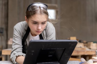 Bir kadın marangozun portresi bir mobilya fabrikasında mobilyalarını yaptığı için tablet üzerindeki tasarımlara bakıyor. bir çok alet ve ahşap ile