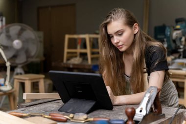 Bir kadın marangozun portresi bir mobilya fabrikasında mobilyalarını yaptığı için tablet üzerindeki tasarımlara bakıyor. bir çok alet ve ahşap ile