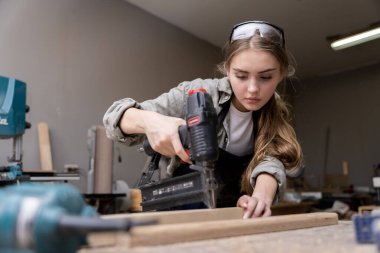 Mobilya fabrikasında mobilya yapmak için alet kullanan bir kadın marangozun portresi. modern araçlarla