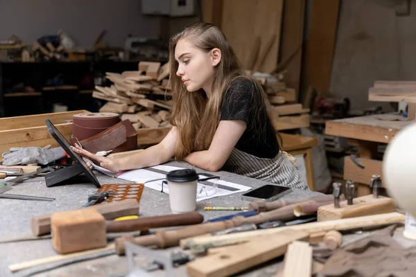一个女木匠的肖像 她在一家家具厂做家具时 看着石碑上的图案 用许多工具和木料 — 图库照片
