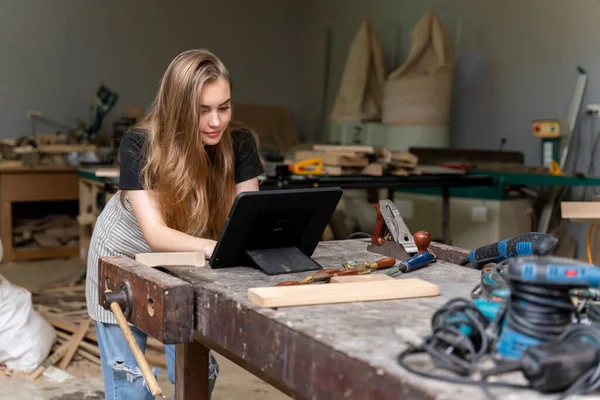 stock image Portrait of a female carpenter looking at designs on a tablet for making her furniture in a furniture factory. with many tools and wood