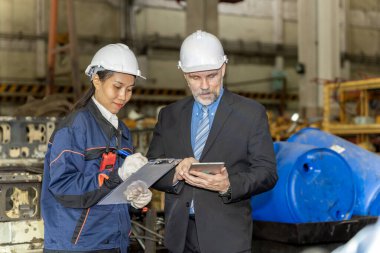 A business man inspects the work of an on-site worker at an old factory for rehearsing train engines.	