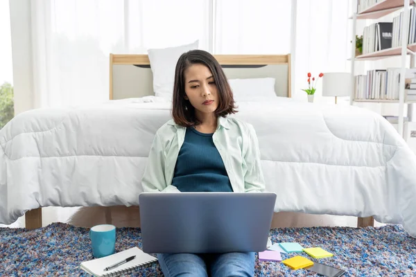 Asian woman working at bedside in bedroom at home with her tablet
