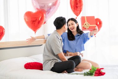 Asian couple Showing love surprise giving flowers or gifts to each other on important occasions such Valentine's Day birthdays or wedding anniversaries with love and warmth in bedroom of their home
