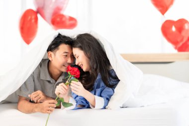 Asian couple Showing love surprise giving flowers or gifts to each other on important occasions such Valentine's Day birthdays or wedding anniversaries with love and warmth in bedroom of their home