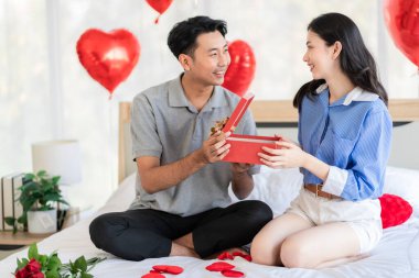 Asian couple Showing love surprise giving flowers or gifts to each other on important occasions such Valentine's Day birthdays or wedding anniversaries with love and warmth in bedroom of their home