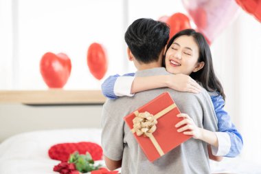 Asian couple Showing love surprise giving flowers or gifts to each other on important occasions such Valentine's Day birthdays or wedding anniversaries with love and warmth in bedroom of their home