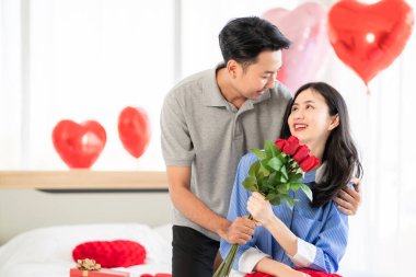 Asian couple Showing love surprise giving flowers or gifts to each other on important occasions such Valentine's Day birthdays or wedding anniversaries with love and warmth in bedroom of their home