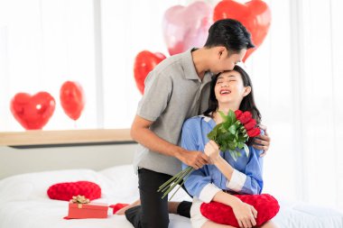 Asian couple Showing love surprise giving flowers or gifts to each other on important occasions such Valentine's Day birthdays or wedding anniversaries with love and warmth in bedroom of their home
