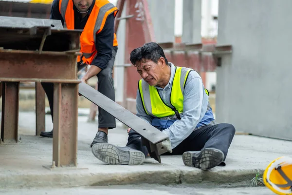 engineer has an accident where steel falls on his leg at work, causing serious leg injuries. and get help from colleagues in the area under construction industrial factory, concept, safe work