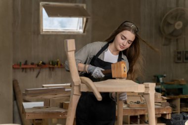 Dişi bir marangoz tasarladığı ve yaptığı sandalyeyi birleştiriyor. Evinde bulunan mobilya fabrikasında.