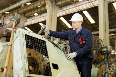 Bir makine fabrikası mühendisi fabrikadaki makineleri tablet veya dizüstü bilgisayarla ve kasten göz kontrolüyle inceliyor. Fabrika büyük ve eski..