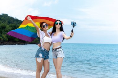 Plajda LGBTQ bayraklı lezbiyen çift, denizde birlikte tatilde mutlu çift.