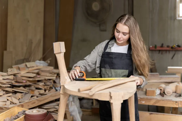 Dişi bir marangoz tasarladığı ve yaptığı sandalyeyi birleştiriyor. Evinde bulunan mobilya fabrikasında.