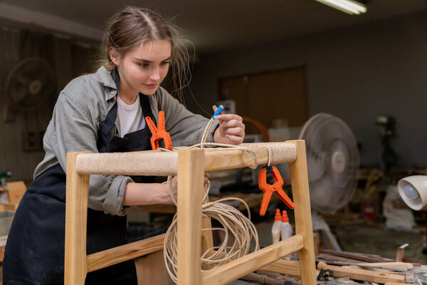 A female carpenter assembling a chair she had designed and built. At the furniture factory found inside her house