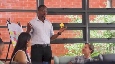Modern bir ofiste, bir ekiple birlikte yeni bir projeyi tartışan genç bir Afrikalı Amerikalının görüntüsü.