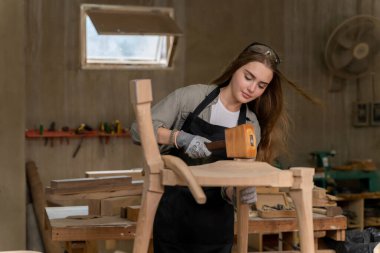 Dişi bir marangoz tasarladığı ve yaptığı sandalyeyi birleştiriyor. Evinde bulunan mobilya fabrikasında.