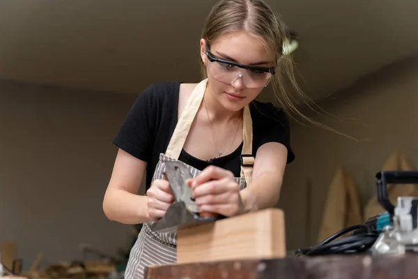 Portrait of a female carpenter using furniture tools in a furniture factory. she is using a planer planing with wood used to create furniture with modern tools