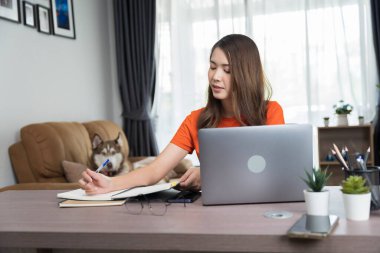 Kıvırcık saçlı Asyalı kadın, bilgisayar ve cep telefonuyla iletişim kanalları, telefon, internet üzerinden müşterileri veya iş arkadaşlarıyla sohbet ediyor.