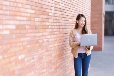 Asyalı kız öğrenci üniversite alanında sınavlara hazırlanıyor. İnternete bağlı cep telefonu ya da dizüstü bilgisayarla iletişim kurun. bir çok bilgi kaynağıyla