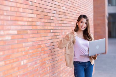 Asyalı kız öğrenci üniversite alanında sınavlara hazırlanıyor. İnternete bağlı cep telefonu ya da dizüstü bilgisayarla iletişim kurun. bir çok bilgi kaynağıyla
