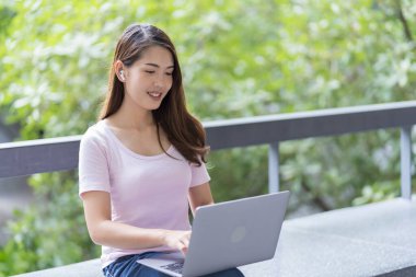 Asyalı kız öğrenci üniversite alanında sınavlara hazırlanıyor. İnternete bağlı cep telefonu ya da dizüstü bilgisayarla iletişim kurun. bir çok bilgi kaynağıyla