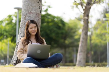 Asyalı kız öğrenci üniversite alanında sınavlara hazırlanıyor. İnternete bağlı cep telefonu ya da dizüstü bilgisayarla iletişim kurun. bir çok bilgi kaynağıyla