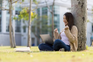 Asyalı kız öğrenci üniversite alanında sınavlara hazırlanıyor. İnternete bağlı cep telefonu ya da dizüstü bilgisayarla iletişim kurun. bir çok bilgi kaynağıyla