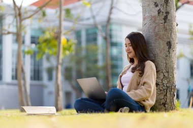 Asyalı kız öğrenci üniversite alanında sınavlara hazırlanıyor. İnternete bağlı cep telefonu ya da dizüstü bilgisayarla iletişim kurun. bir çok bilgi kaynağıyla