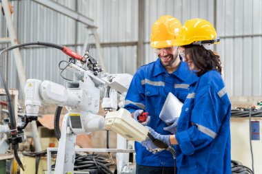 Erkek ve kadın mühendislerden oluşan bir ekip bilgisayar kontrollü çelik kaynaklama robotlarını incelemek için toplanıyor. Provalar ve kullanım için kurulum planı.