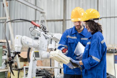 Erkek ve kadın mühendislerden oluşan bir ekip bilgisayar kontrollü çelik kaynaklama robotlarını incelemek için toplanıyor. Provalar ve kullanım için kurulum planı.