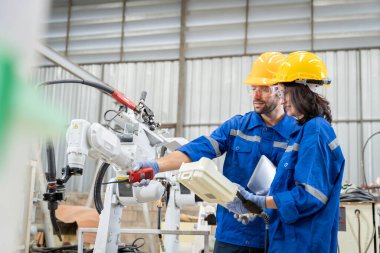Erkek ve kadın mühendislerden oluşan bir ekip bilgisayar kontrollü çelik kaynaklama robotlarını incelemek için toplanıyor. Provalar ve kullanım için kurulum planı.