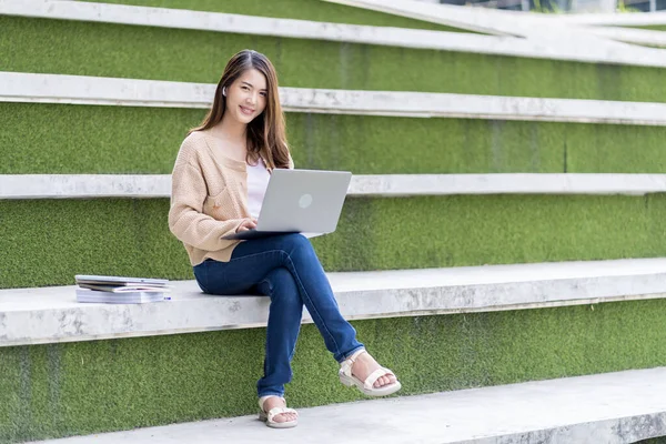 Asyalı kız öğrenci üniversite alanında sınavlara hazırlanıyor. İnternete bağlı cep telefonu ya da dizüstü bilgisayarla iletişim kurun. bir çok bilgi kaynağıyla