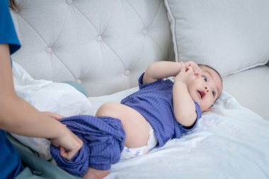 Bir kadın kucağında bebekle kanepede oturuyor. Bebek mor bir elbise giyiyor.