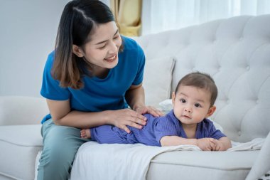 Bir kadın kucağında bebekle kanepede oturuyor. Bebek mor bir elbise giyiyor.