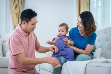 Bir adam ve bir kadın aralarında bir bebekle kanepede oturuyorlar. Bebek mor bir kıyafet giyiyor. Sahne sıcak ve sevgi dolu, çünkü aile birlikte kaliteli zaman geçiriyor.