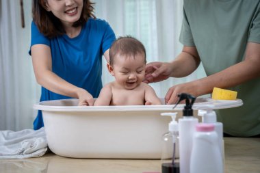 Anne ve baba, bebeklerini küvette yıkamak için birbirlerine yardım ediyorlar. Resimde herkes mutlu görünüyor..
