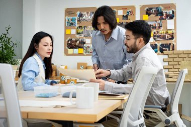 Üç adam ve bir kadın duvarında beyaz bir tahtayla bir masanın etrafında oturuyorlar. Bir şey tartışıyorlar ve adamlardan biri elinde bir kağıt parçası tutuyor.