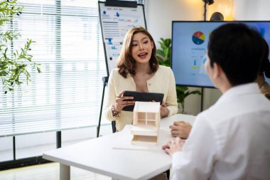 Yüzünde bir gülümsemeyle beyaz bir tahtanın önünde duran bir kadın. O, bir sandalyede oturan diğer iki kişiyle konuşuyor. İşbirliği ve takım çalışması kavramı