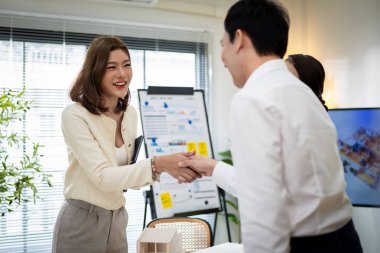 Yüzünde bir gülümsemeyle beyaz bir tahtanın önünde duran bir kadın. O, bir sandalyede oturan diğer iki kişiyle konuşuyor. İşbirliği ve takım çalışması kavramı