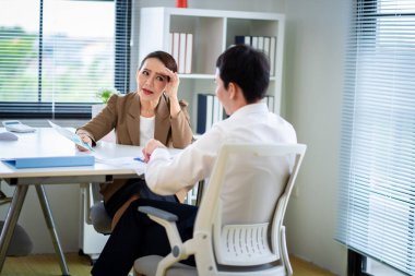 İki kişi bir iş ortamında bir masada oturmuş bir şey tartışıyorlar. İçlerinden biri bir kağıt parçası tutuyor.