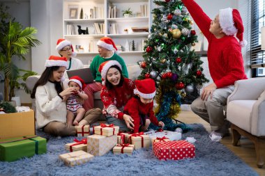 Noel günü Asyalı bir aile. Hediye ve turuncu ışıklarla dolu Noel temalı bir odada herkes mutlu..