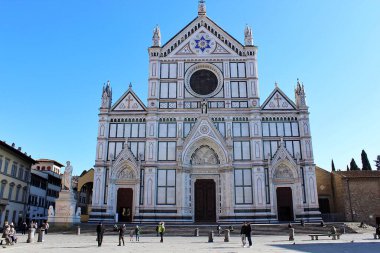 Ziyaretçiler, Floransa 'daki Santa Croce Bazilikası' nın çarpıcı mimarisine hayran. Güzel bir günde güneşle dolu açık mavi bir gökyüzünün altında güneşleniyorlar..