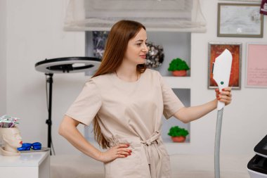 Güzellik uzmanı yüz ve cilt gerdirme işlemi ve saç aldırma için ultrason cihazı tutuyor. Genç kadın kozmetolog klinikte modern kozmetoloji ekipmanları kullanıyor..