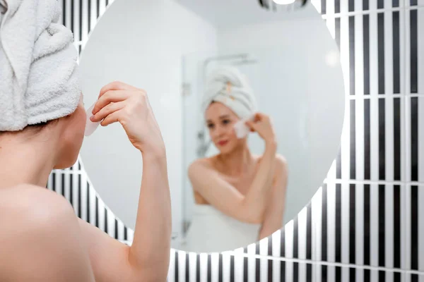 バスルームでの美容朝のルーチン中にピンクの石英スクレーパーで顔のマッサージを行う白いタオルを身に着けている若い美しい女性 アンチエイジング治療とスキンケアのコンセプト — ストック写真
