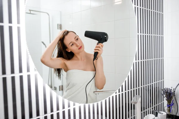 若い女性は ヘアドライヤーで髪を乾燥させ スタイリング 現代のバスルームのインテリアで髪型を作ります 朝のシャワー後の美容ルーチン — ストック写真