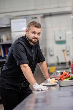 Professional chef in uniform cut fresh vegetables in kitchen. Cook man cooking delicious garnish for clients in restaurant. Culinary concept