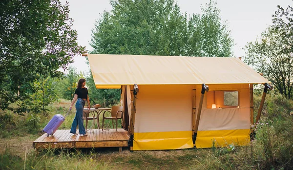 Woman traveler with luggage moving towards bedroom of cozy glamping house. Luxury camping tent for outdoor summer holiday and vacation. Lifestyle concept