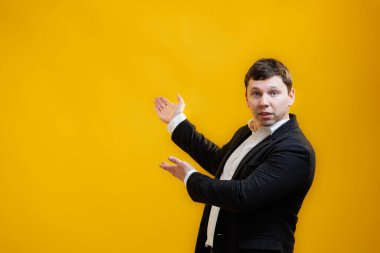 Handsome businessman wearing suit standing pointing hands aside on mock up copy space on yellow studio background